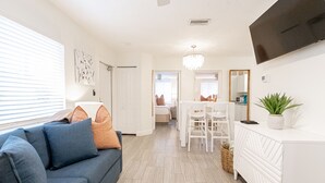 A modern living room with a sofa, a dining table, and a TV mounted on the wall. - Siesta Key Beachside Villas (Siesta Key)