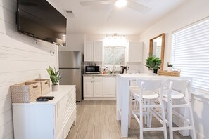 A modern kitchen with white cabinetry, a flat-screen TV, a refrigerator, and a dining area with white chairs.