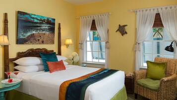 A hotel room with a bed, a chair, a painting, a lamp, and a window with curtains.
