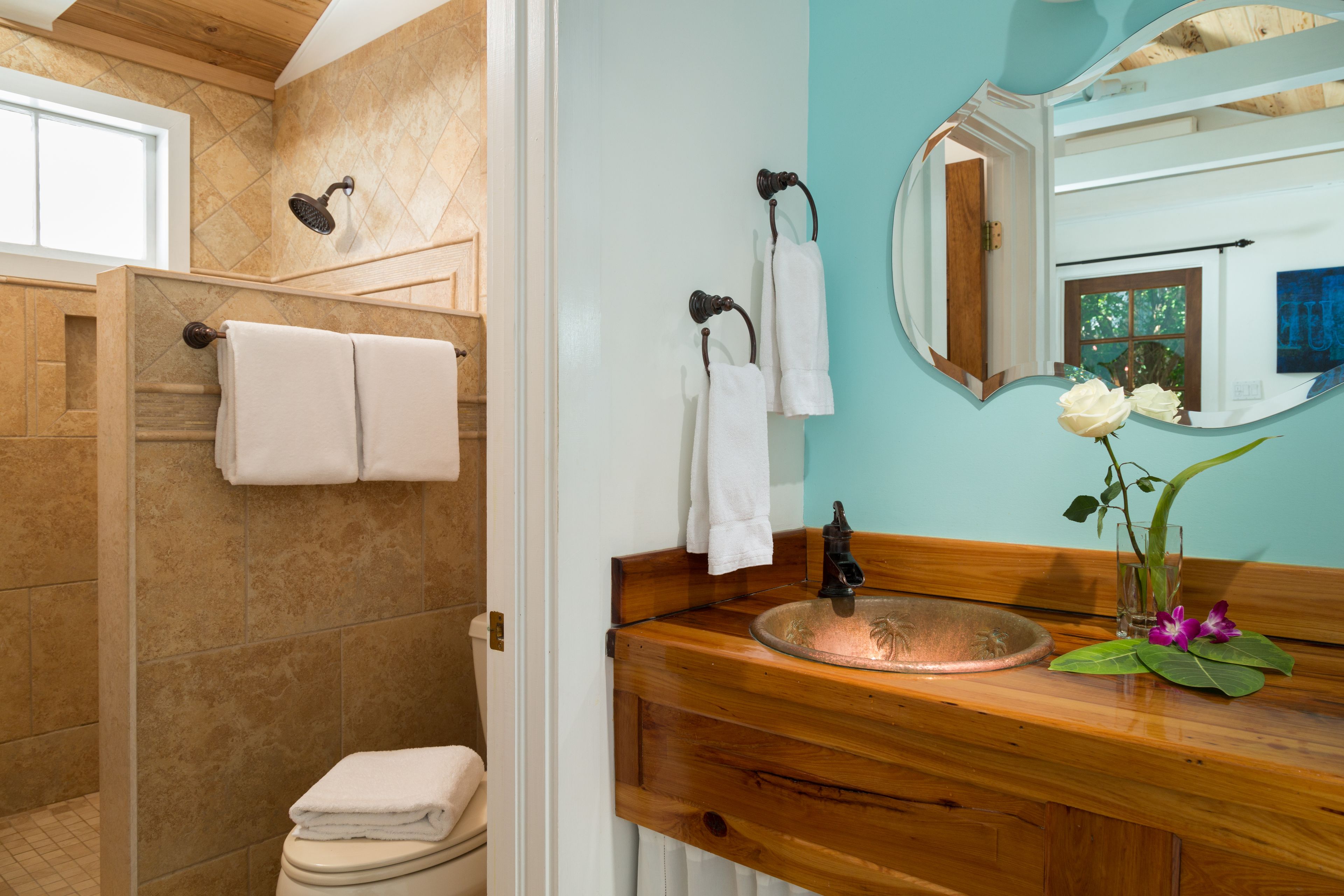 Un baño con tocador de madera, lavamanos, espejo y zona de ducha.