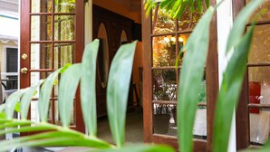 Una puerta de madera con paneles de vidrio, que da acceso a un espacio interior con muebles y plantas.