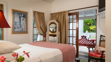 Habitación de hotel con cama, espejo, silla y puerta que da a un balcón con plantas.