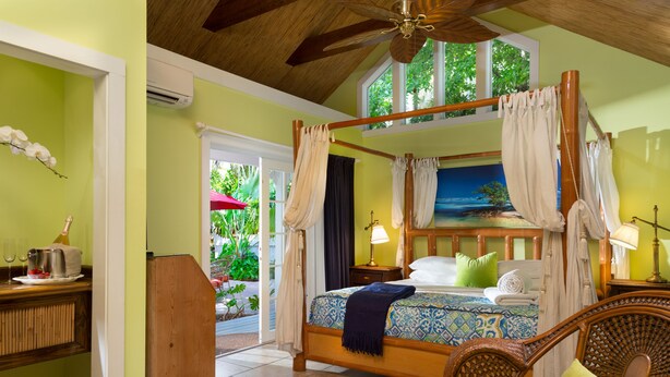 Un dormitorio con cama con dosel, un escritorio de madera, sillas de mimbre y vistas al exterior.