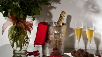 Une table avec un vase de fleurs, une bouteille de champagne, deux coupes de champagne et des fraises enrobées de chocolat.