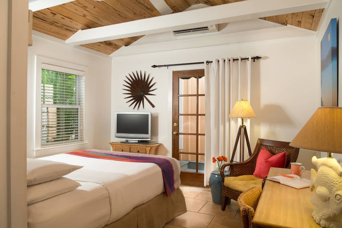 A hotel room with a bed, a television, a lamp, a chair, and a decorative wall piece.