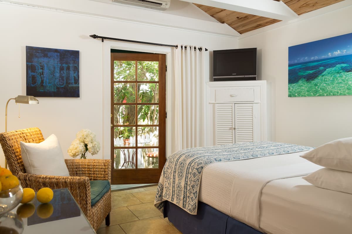 A bedroom with a bed, a television, a wicker chair, a window with curtains, and a painting on the wall.