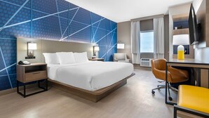 A hotel room with a large bed, bedside tables, a desk with a chair, a TV, and a window with curtains.