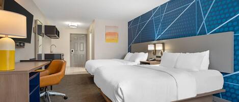 A hotel room with a bed, desk, chair, and a wall with a geometric pattern.