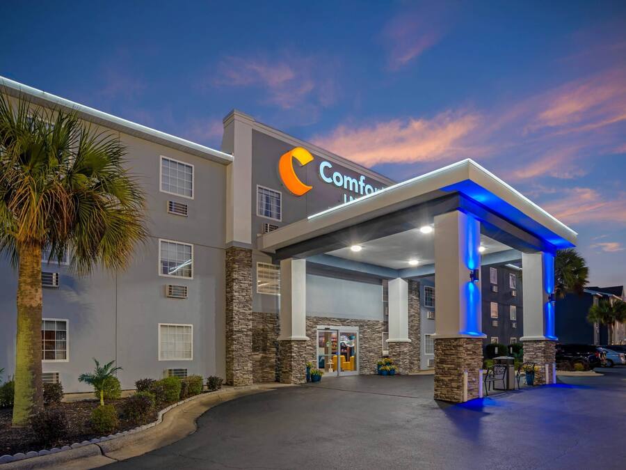 A hotel with a modern design, featuring a prominent 'Comfort Inn' sign, a covered entrance, and a parking area.