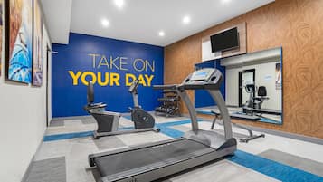 Un gimnasio con cinta de correr, elíptica y pesas, una pared azul motivadora y un espejo.