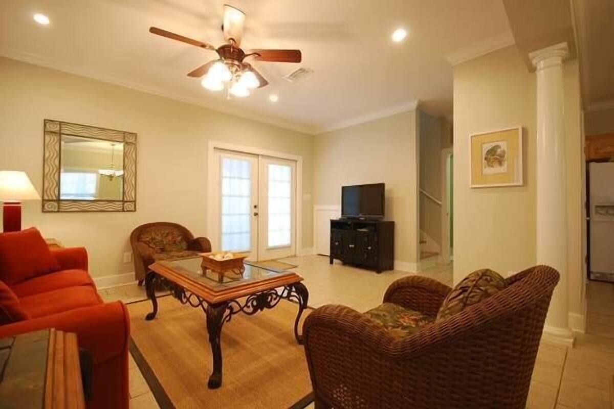 A living room with a ceiling fan, a television, wicker furniture, and a large mirror.