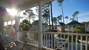 A covered porch with white railings, wooden benches, and a view of multiple houses with green roofs. - Purple Parrot Village (Pensacola)
