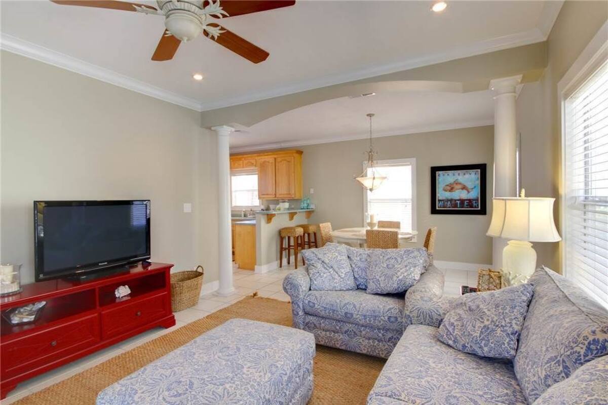 A living room with a television, red entertainment unit, patterned sofa, and ottoman.