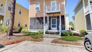 A two-story house with a front porch, a garage, and a small front yard with landscaping. - Purple Parrot Village (Pensacola)