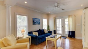 A living room with a blue sofa, a yellow armchair, a coffee table, and a ceiling fan. - Purple Parrot Village (Pensacola)