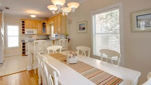 A bright kitchen with white cabinets, a microwave, and a dining area with a white table and chairs. - Purple Parrot Village (Pensacola)
