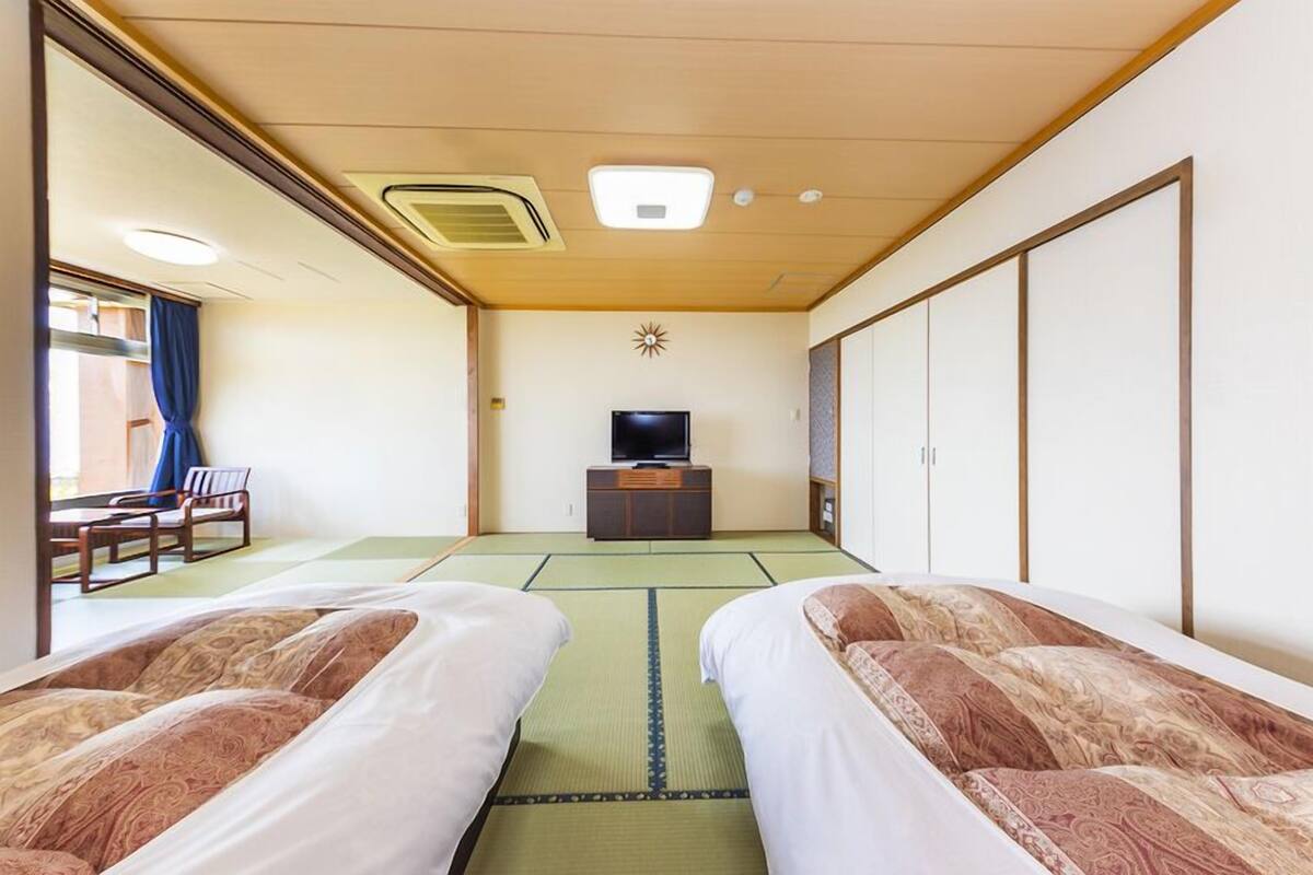 A hotel room with tatami mats, two beds, a television, and a sliding door.