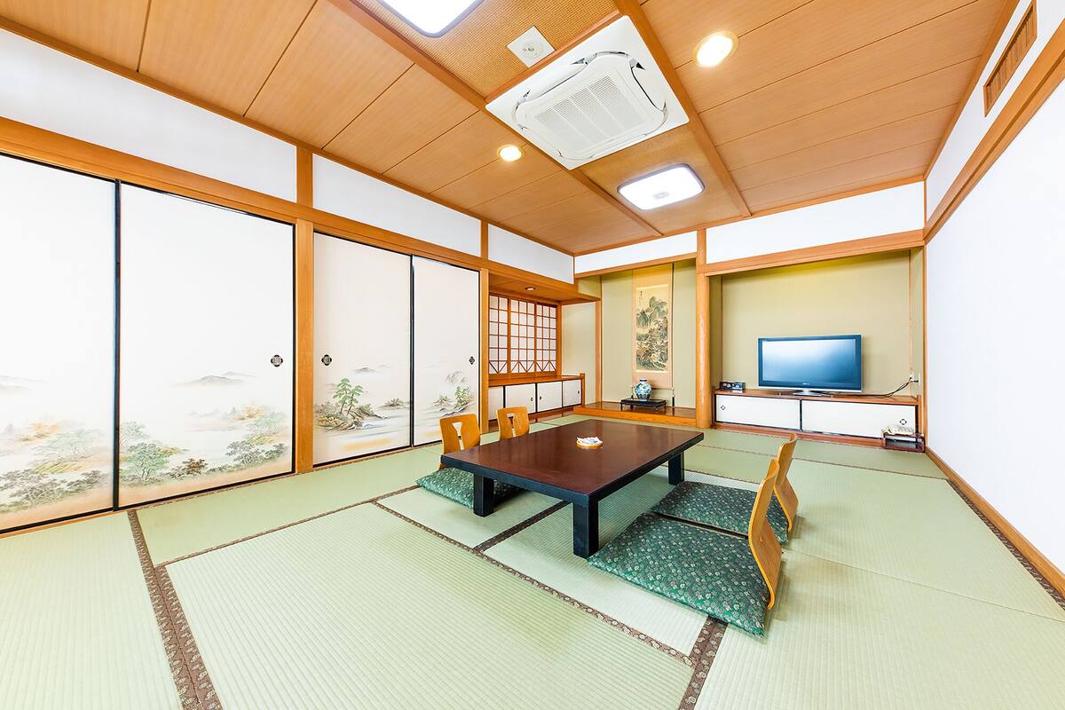 A traditional Japanese-style room with tatami flooring, a low table, sliding doors, and a television on a stand.