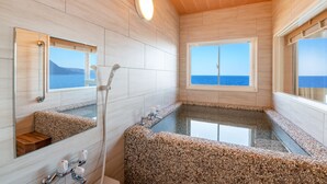 Un baño con una bañera grande, ducha y ventana con vista al mar.