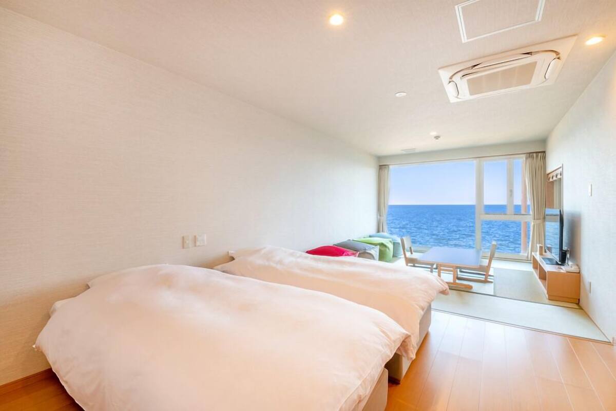 A room with two beds, a small table, and a view of the sea.