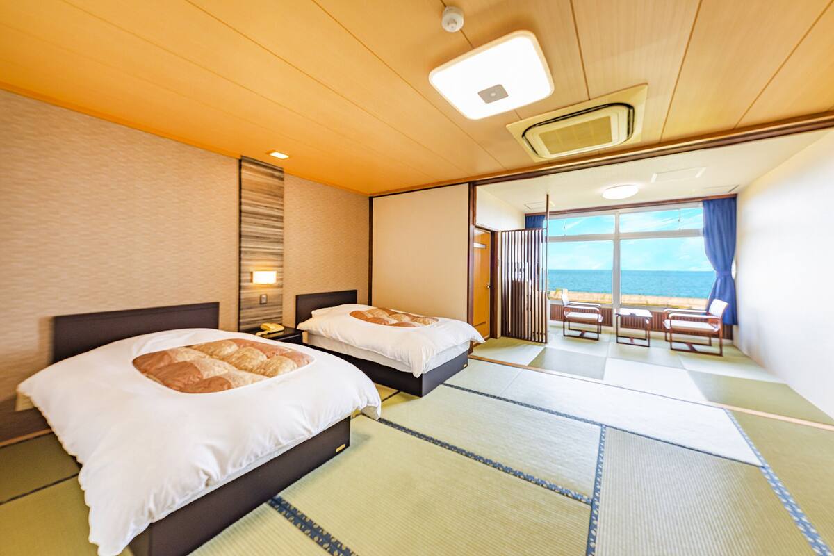 A hotel room with two beds, a view of the sea, and a balcony with chairs.