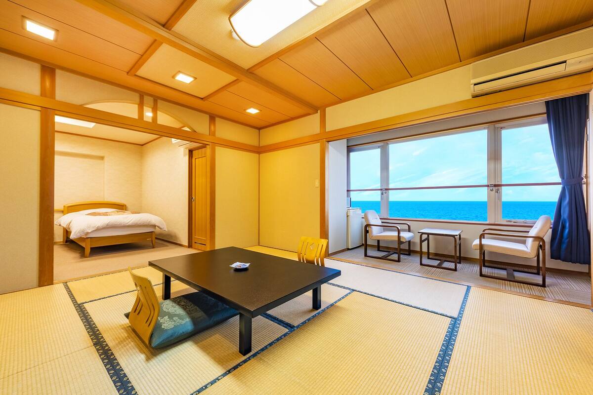 A room with a bed, a table, and a view of the sea.
