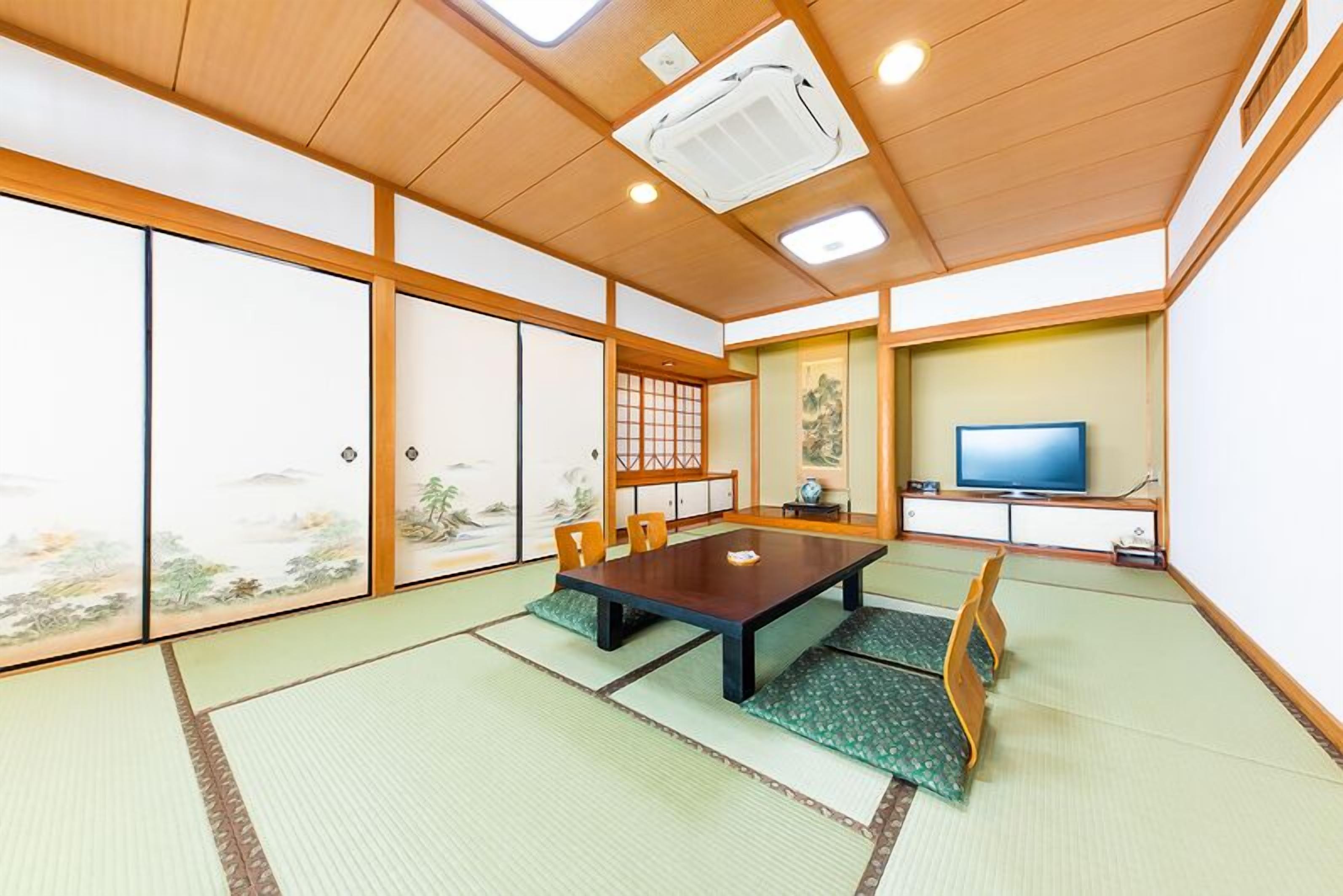 A traditional Japanese room with tatami flooring, a low table, chairs, sliding doors, and a television.