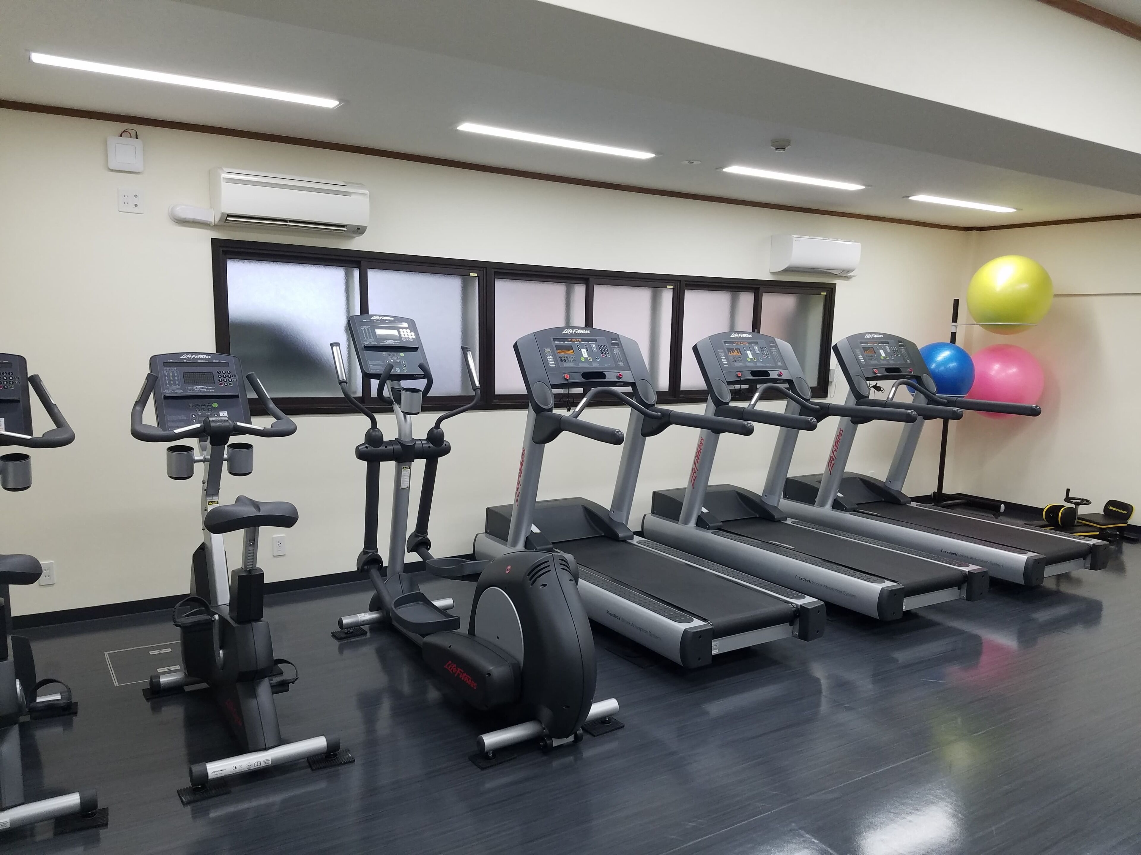 A gym with treadmills, elliptical machines, and exercise balls.