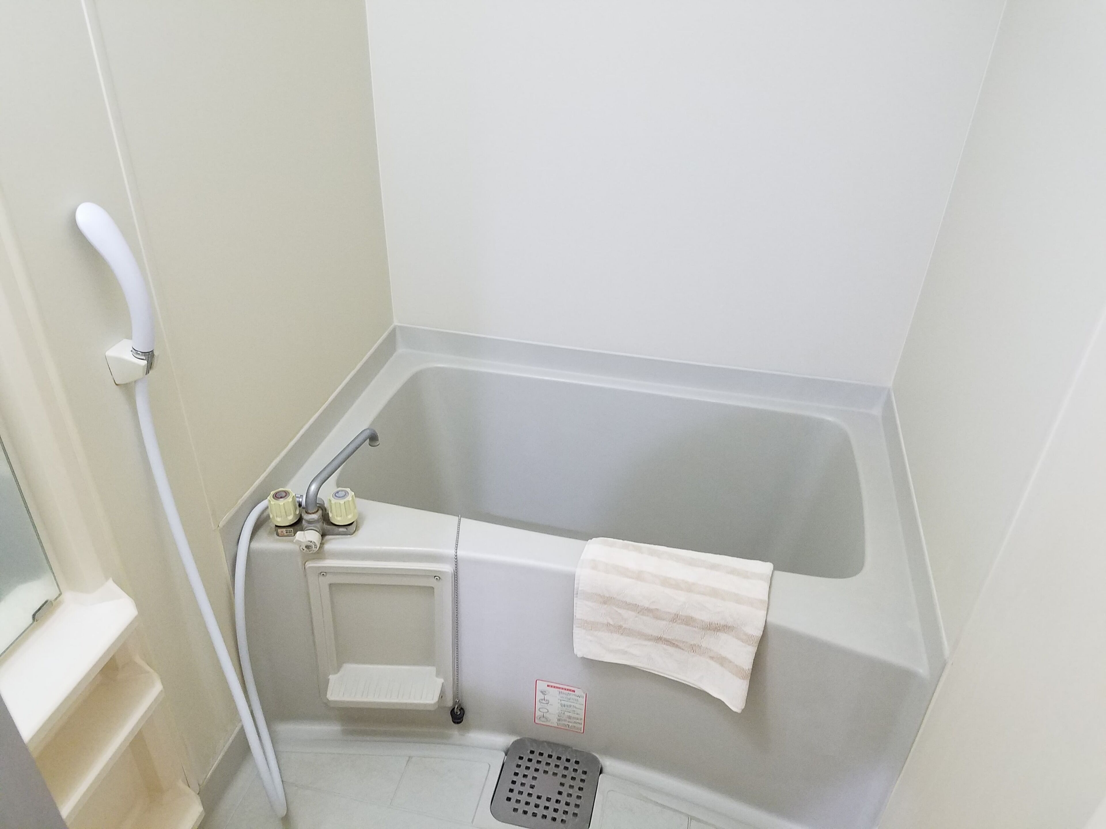 A small, white bathroom with a bathtub, a shower, and a towel hanging on the wall.