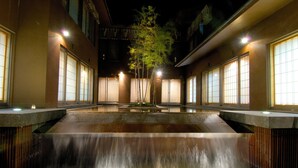 A serene indoor water feature with a central waterfall, flanked by buildings with large windows and warm lighting. - Hoshino Resorts KAI Matsumoto (Matsumoto)