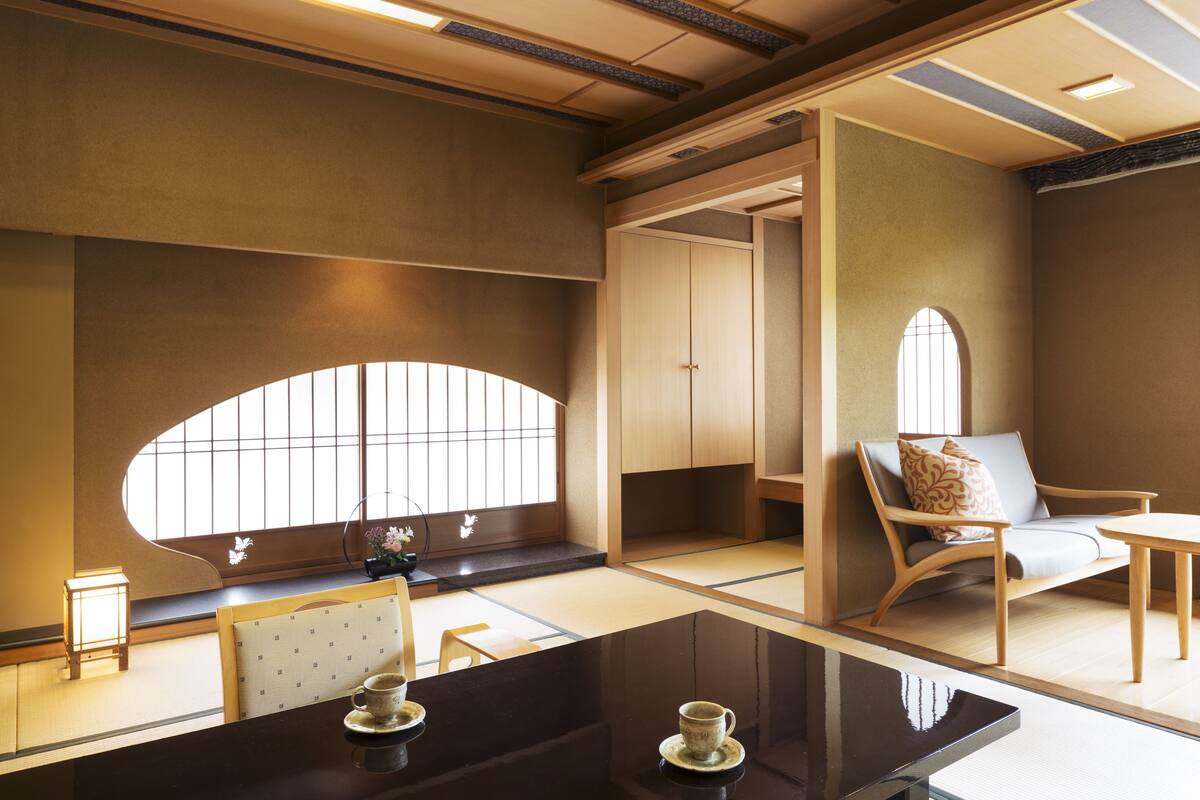 A traditional Japanese room with tatami flooring, a low table with a cup, a cushioned chair, and a window with a view.