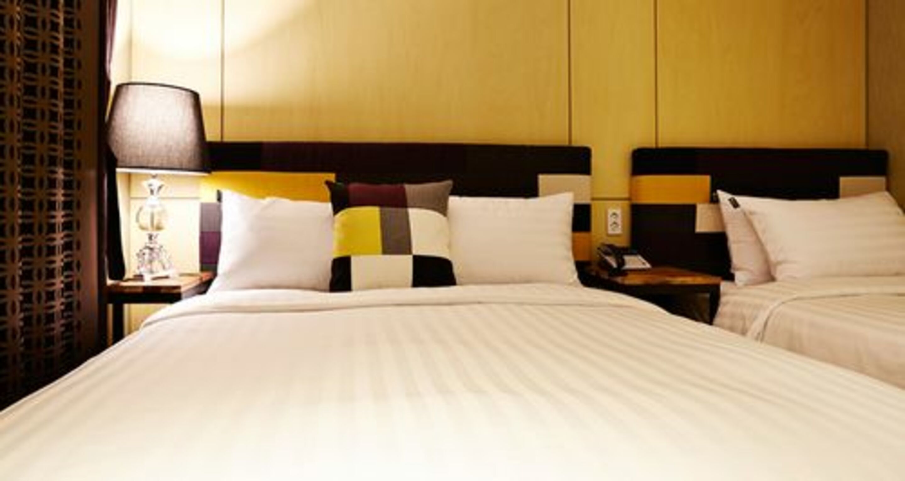 A hotel room with two beds, a nightstand with a lamp, and a patterned wall.