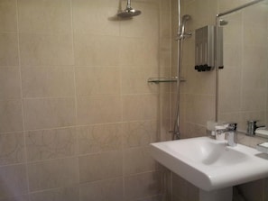 A bathroom with beige tiled walls, a white sink, and a shower with a handheld showerhead. - Hotel Namoo (Cheongju)