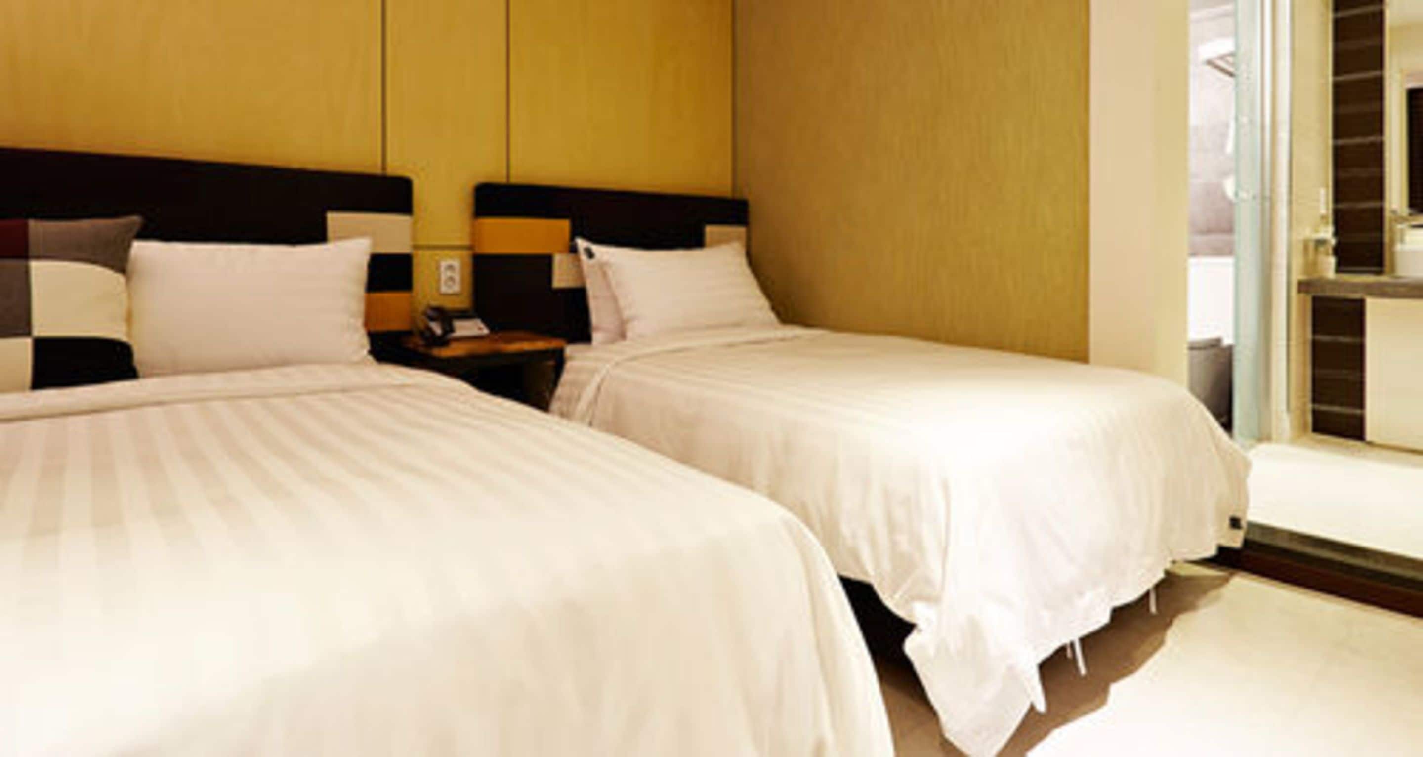 A hotel room with two beds, a nightstand, and a window with a view.