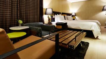 Una habitación de hotel con una cama, un sofá, una pequeña mesa redonda y un banco.
