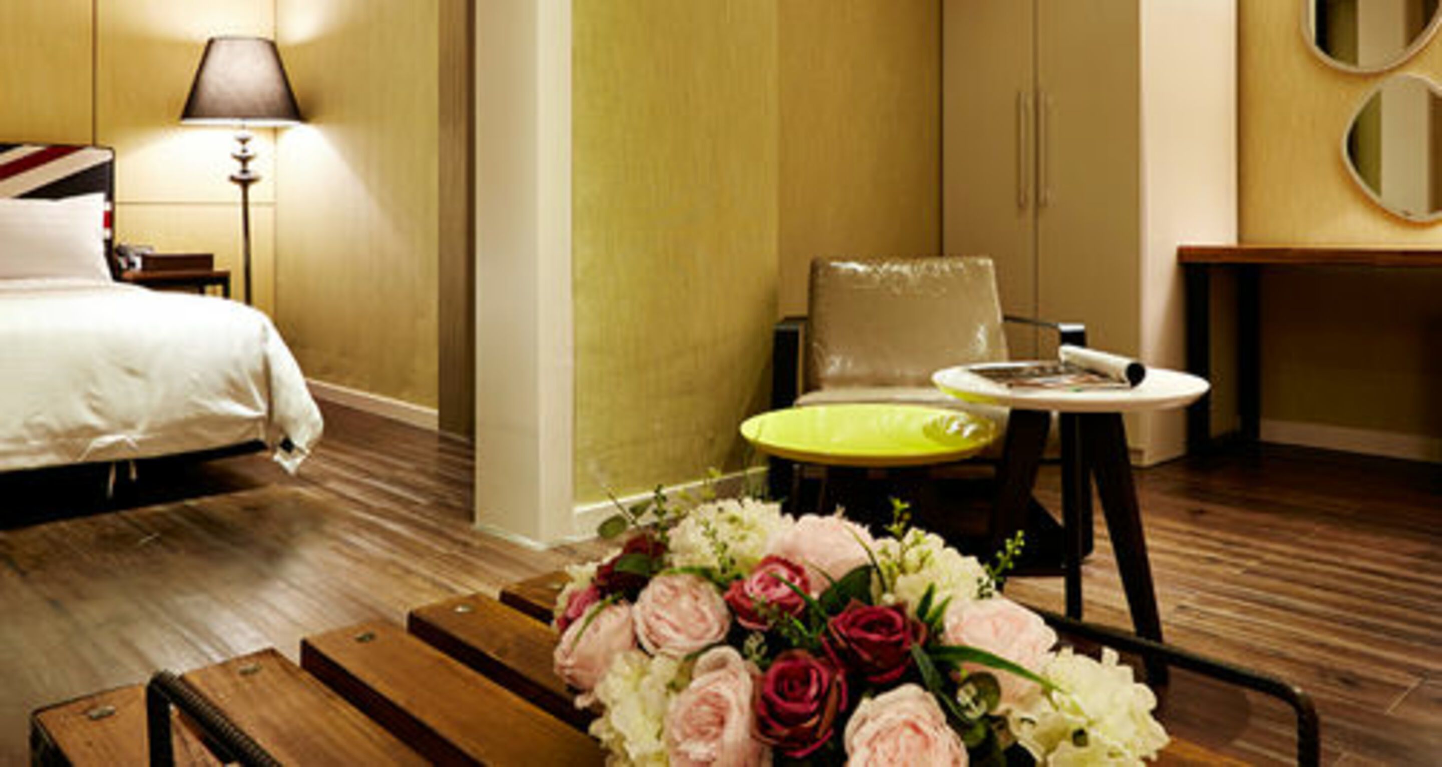 Une chambre d’hôtel avec un lit, une chaise, une petite table et un vase de fleurs.