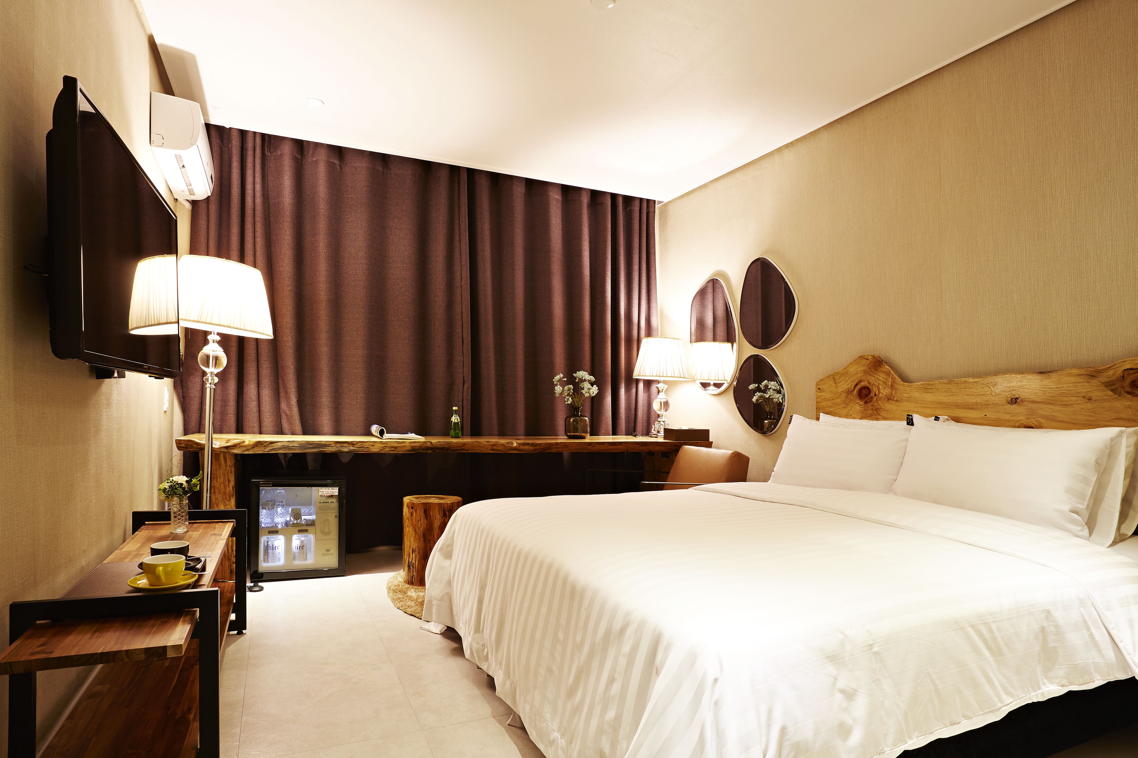 Habitación de hotel con cama, escritorio, silla, refrigerador pequeño, lámpara y espejo.