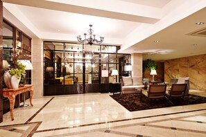A spacious lobby with a chandelier, a seating area with a coffee table, and a view into a restaurant or dining area. - Hotel Namoo (Cheongju)