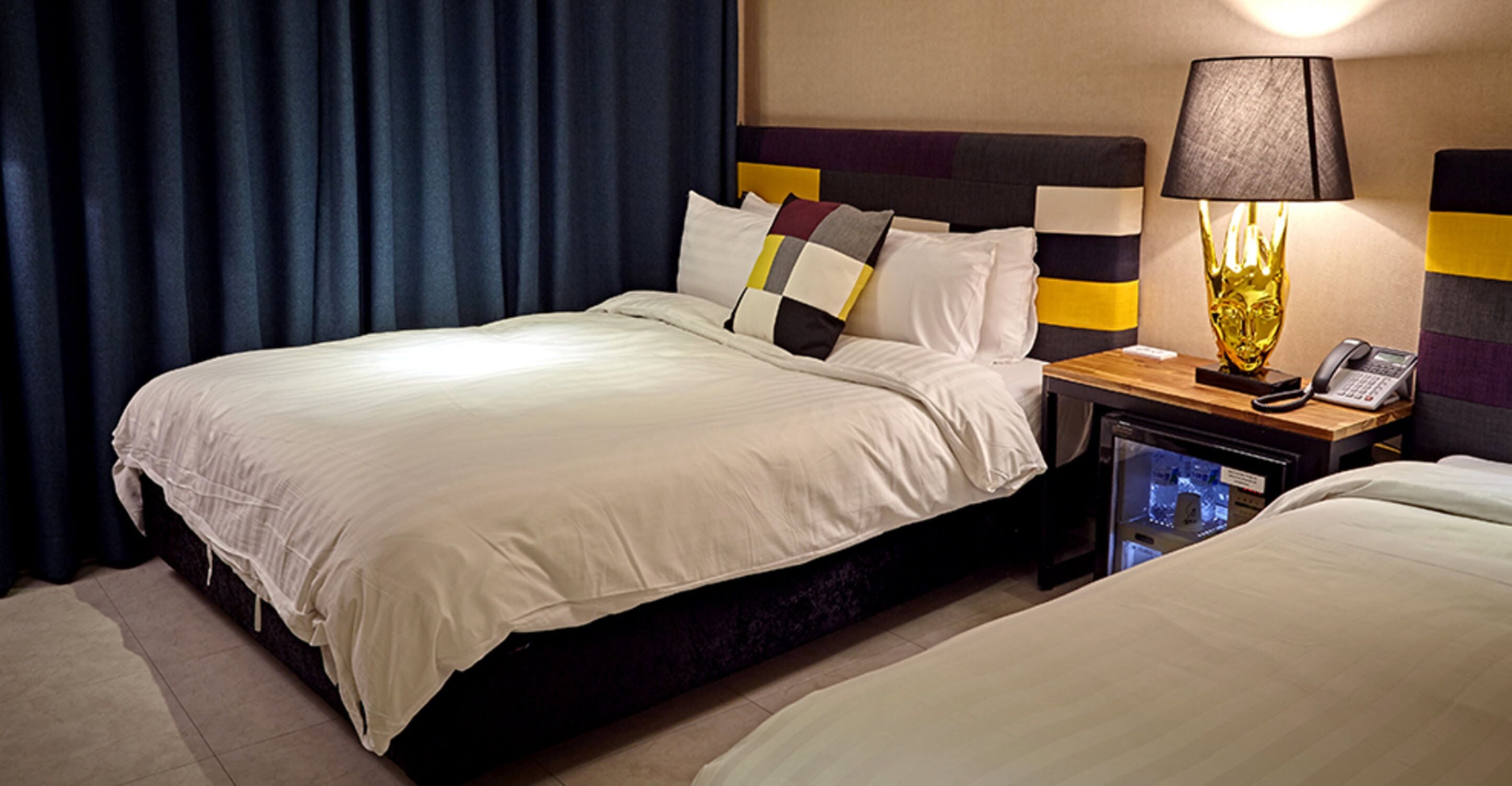 Ein Hotelzimmer mit zwei Betten, einem Nachttisch mit Lampe, einem Telefon und einer Minibar.