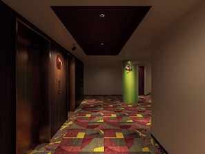 A hallway with a patterned carpet, a wooden door, a green pillar, and a red door at the end.