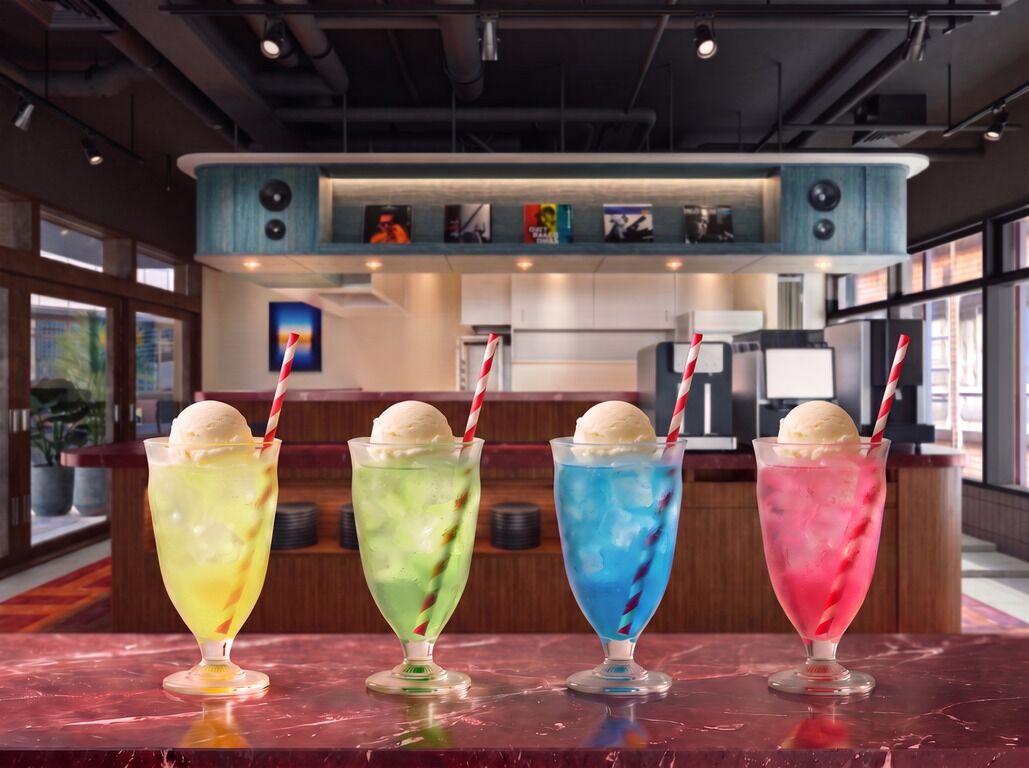 Zona de bar con cuatro bebidas de colores y una barra con un menú.