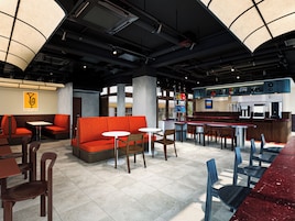Interior moderno de restaurante com disposição de assentos, área de bar e um painel de cardápio visível.