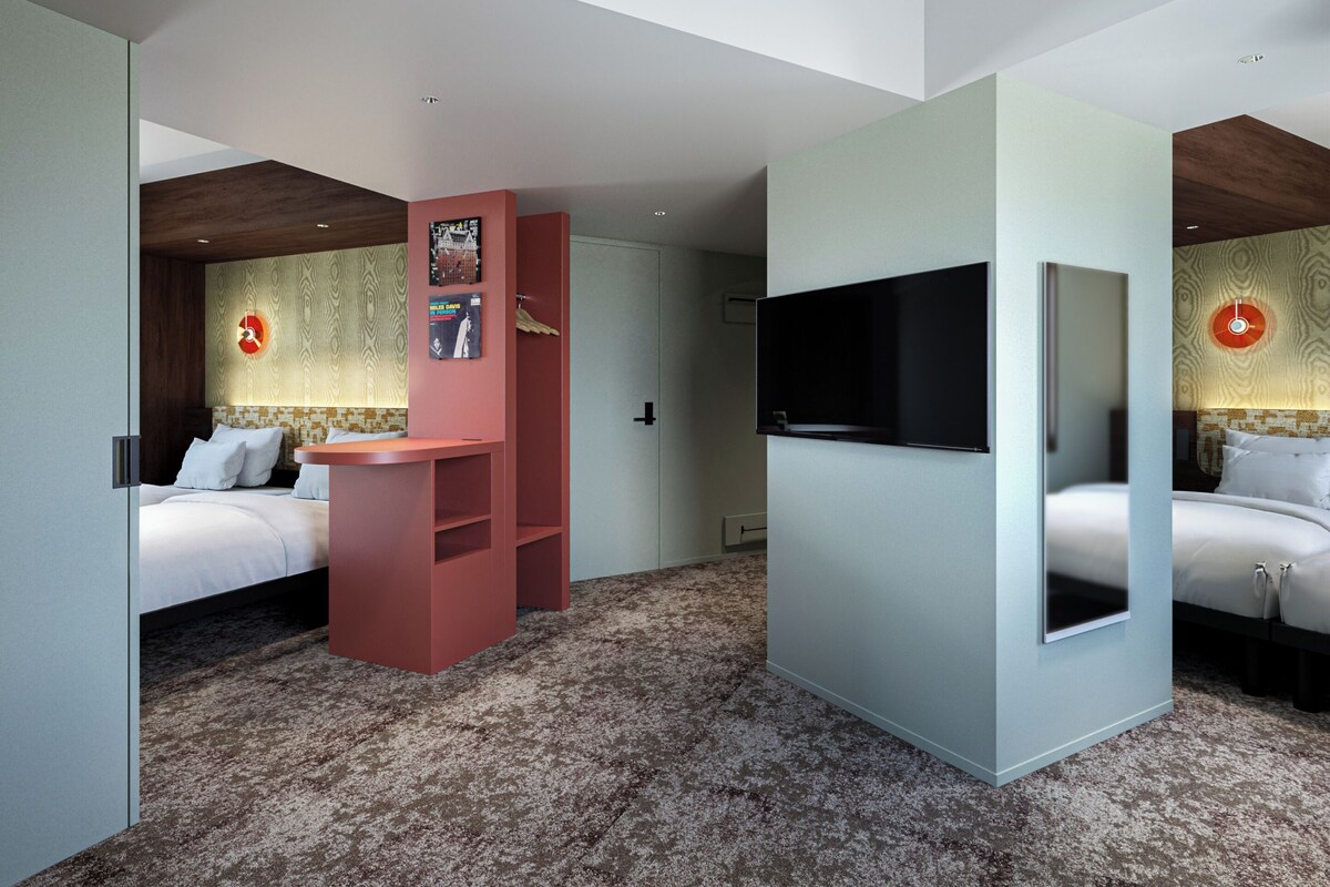 Une chambre d’hôtel moderne avec un grand lit, un téléviseur fixé au mur et une bibliothèque rouge au design original.