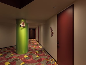 Un corridoio di un albergo con una moquette fantasia, una colonna verde e una porta rossa.