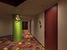 A hotel corridor with a patterned carpet, a green pillar, and a red door.