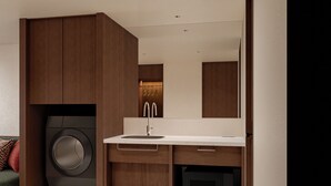 Une cuisine compacte équipée d’un lave-linge intégré, d’un four à micro-ondes et d’un évier avec un robinet moderne.