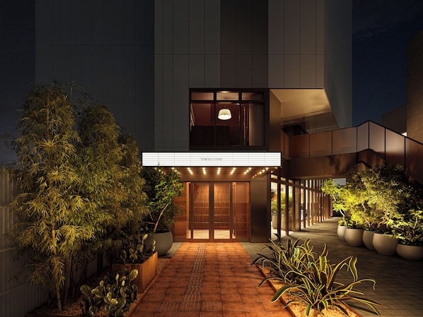 L’entrée d’un hôtel au design moderne, avec une enseigne bien visible et un chemin menant à l’entrée.