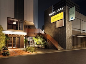 A modern hotel building with a sign that reads 'TOKYU STAY' and a welcoming message.