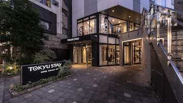 Welcome to Tokyo Stay Hotel, featuring a sleek two-story design with a glass facade and a beautifully landscaped entrance area.