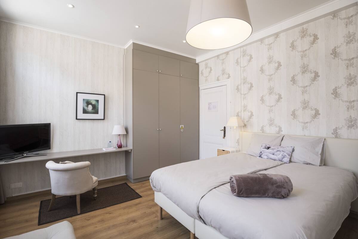 A modern hotel room with a bed, a desk, a television, and a wardrobe.